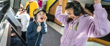 Two children cheer at an exhibit while wearing headphones.